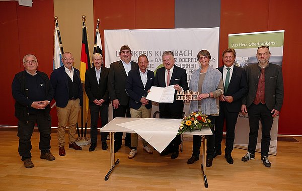 Personen stehen hinter einem Tisch. Eine Person hält die Gründungsurkunde in den Händen.